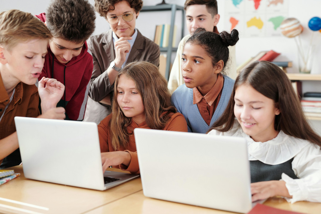 crianças com computador e professora atras